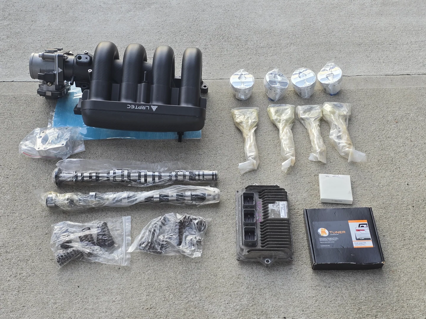 Una colección completa de piezas para el motor del Honda Fit, incluyendo pistones y bielas forjadas, levas, resortes, intake manifold de carbono, throttle body, ECU y KTuner.