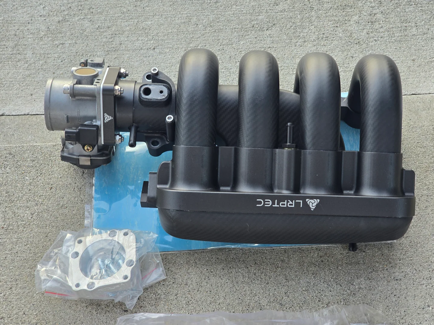 Un intake manifold LRPTech de fibra de carbono conectado a un throttle body electrónico grande para Honda Fit.