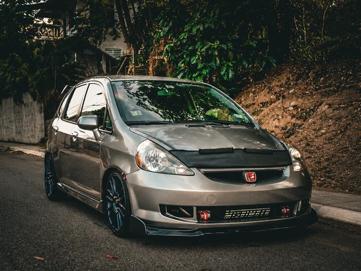 El antiguo Honda Fit GD3 gris y turbo de Harry, estacionado en una carretera de Puerto Rico con el intercooler visible.