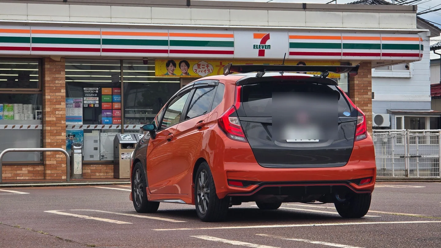Vista trasera del Honda Fit anaranjado terminado con baúl y ala GT de carbono, y la tablilla ocultada.