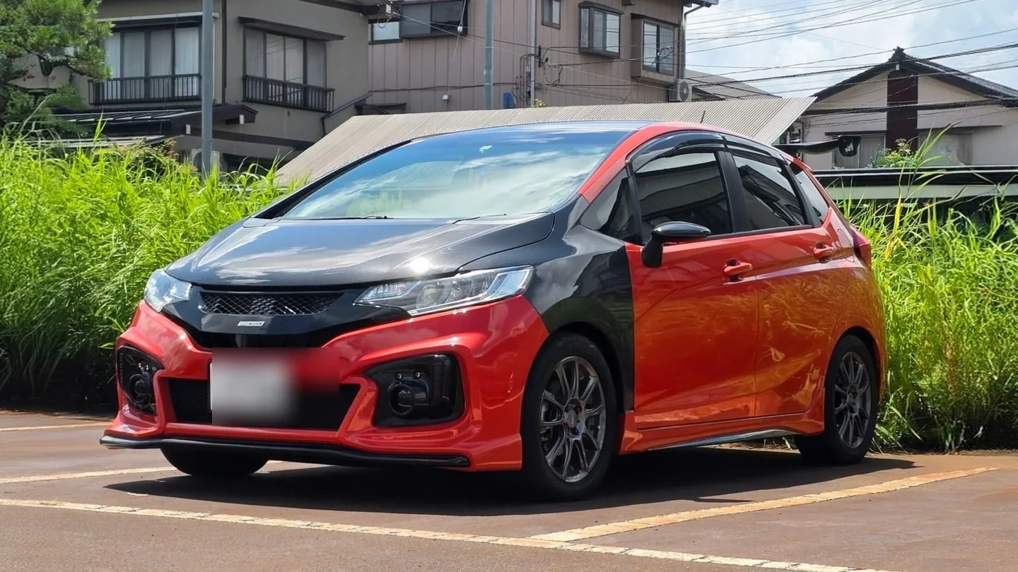 Honda Fit GK5 Sunset Orange II con bonete y guardalodos de wet carbon, fotografiado en Japón con la tablilla ocultada.