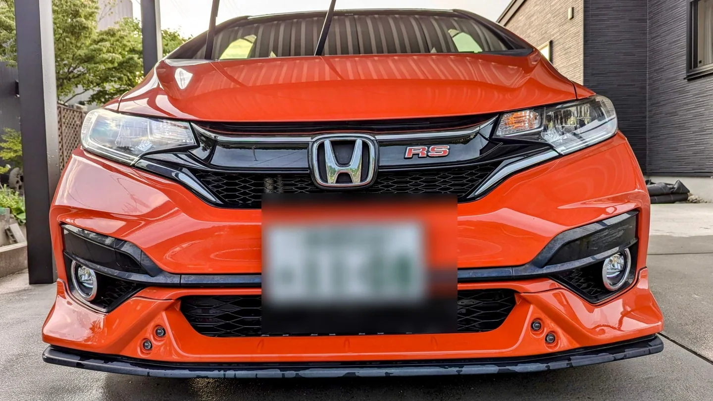 El Honda Fit GK5 anaranjado antes de la conversión exterior a fibra de carbono, con bonete y parrilla originales y la tablilla ocultada.