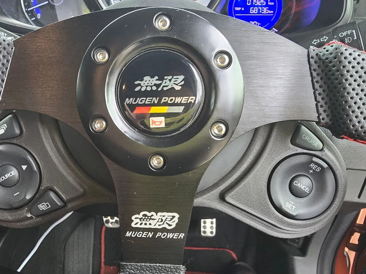 Guía Mugen en un Honda Fit con los controles originales de audio y cruise control relocalizados a sus lados.
