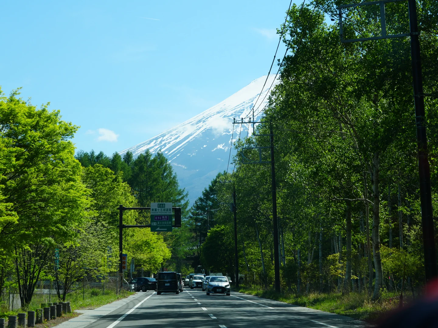 Snow-covered Mount Fuji rises beyond a green roadside on the drive toward Fuji Speedway.