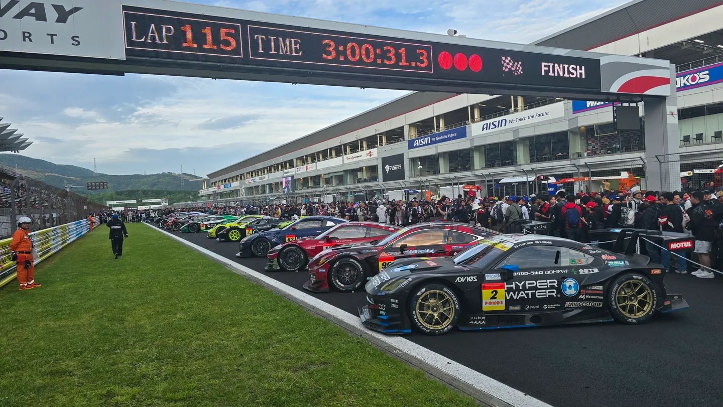 GT300 cars line the Fuji Speedway pit straight beneath a display showing 115 laps and the finish of the three-hour race.