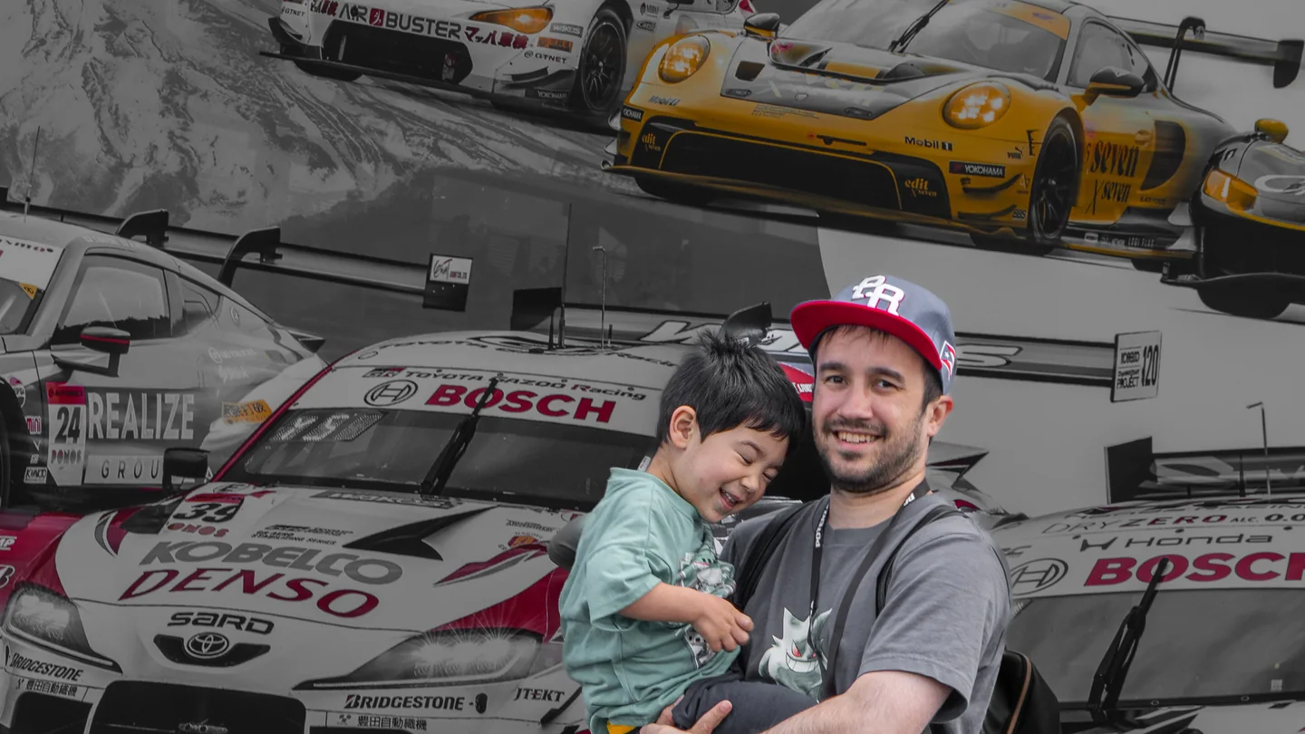Harry holds his smiling youngest son in front of a display filled with SUPER GT race cars at Fuji Speedway.