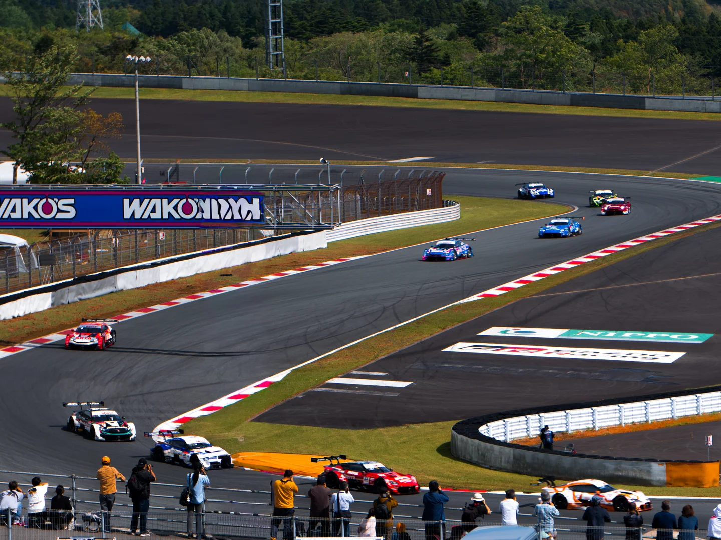 A group of GT500 and GT300 race cars moves through a corner at Fuji Speedway during the three-hour race.