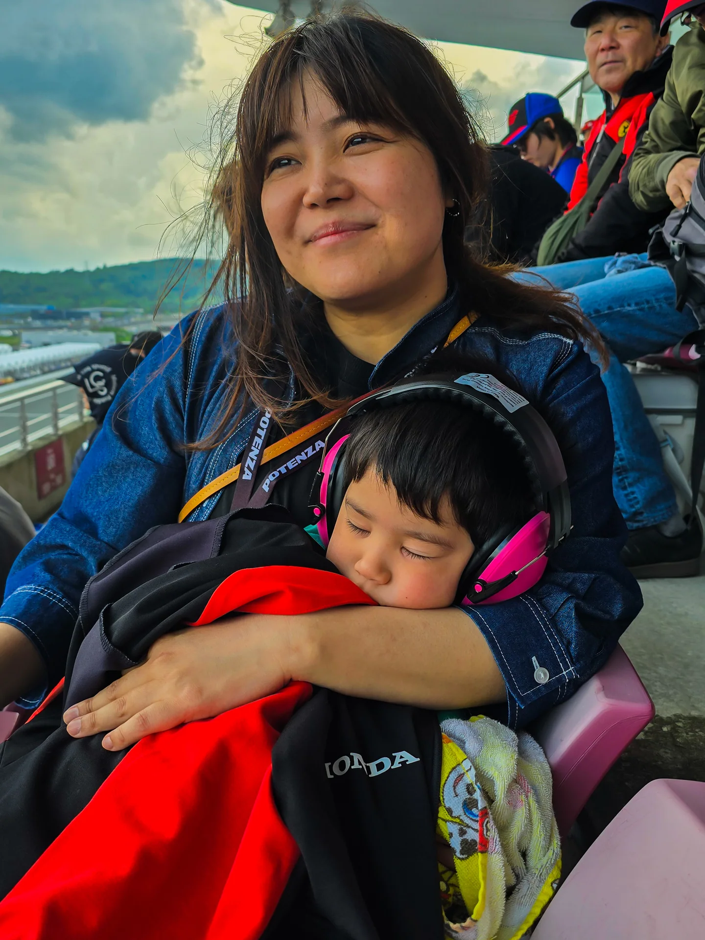 Harry's wife sits in the Fuji Speedway grandstand while their youngest son sleeps on her lap wearing hearing protection.