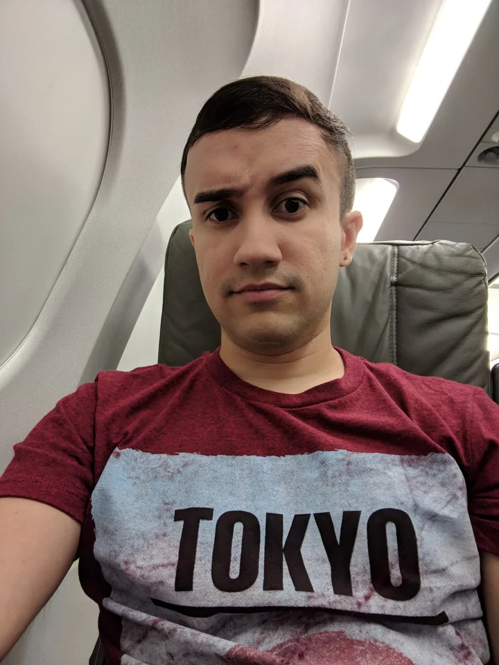 Harry sits alone on an airplane wearing a shirt with Tokyo printed across it.