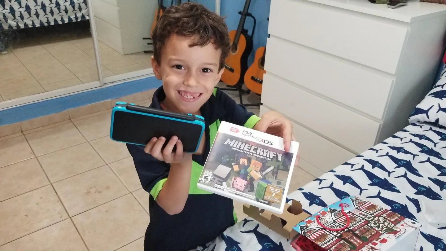 A seven-year-old boy smiles while holding a handheld game system and a game.