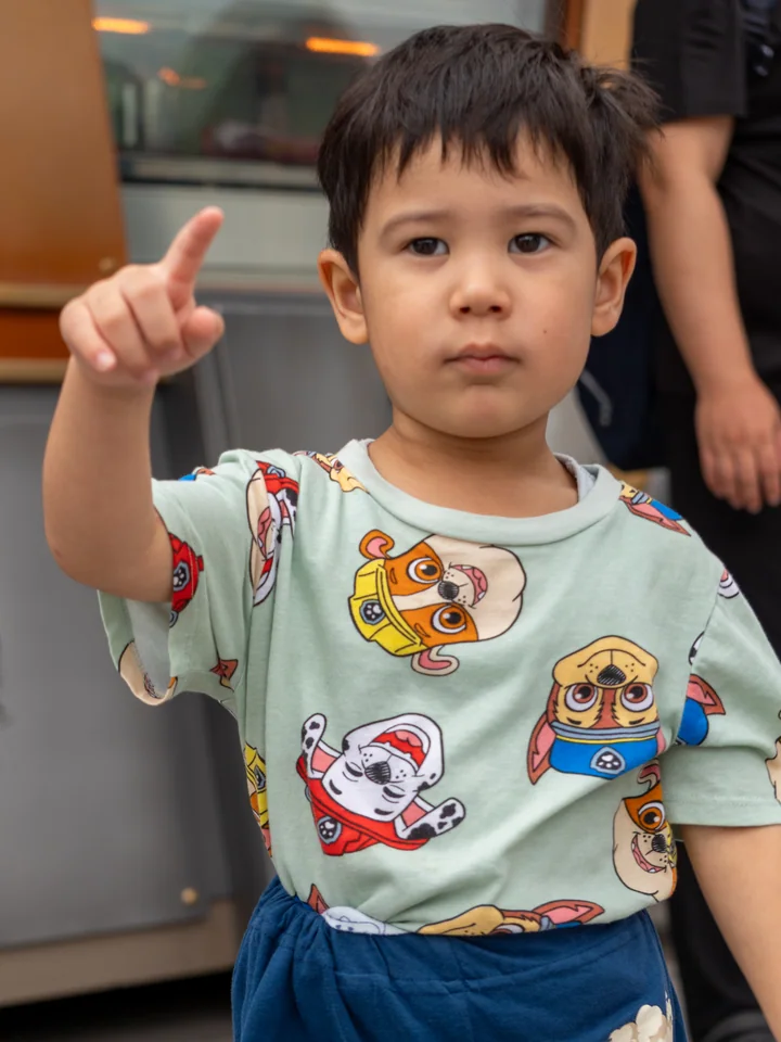El hijo menor señala hacia adelante con autoridad mientras lleva una camisa cubierta de perritos animados.